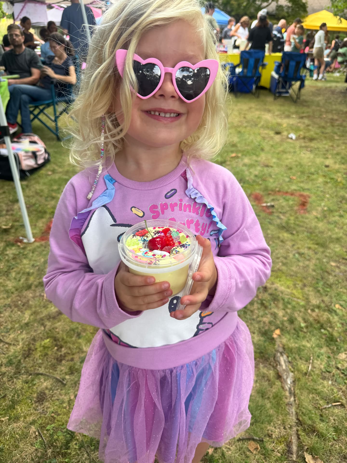A smiling guest in heart sunglasses holding a cup of custom slime sundae with sprinkles and a cherry
