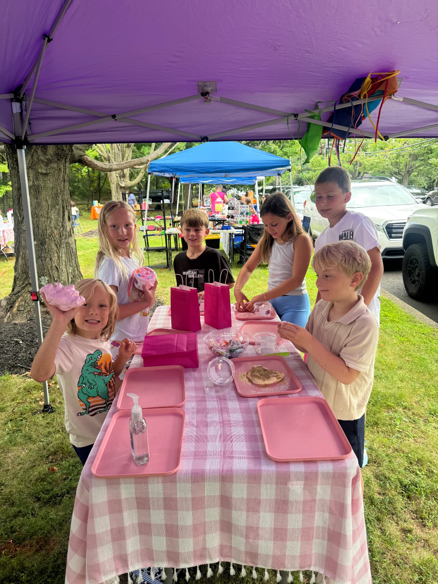 Kids gathered around the table making slime together under a canopy at an outdoor party